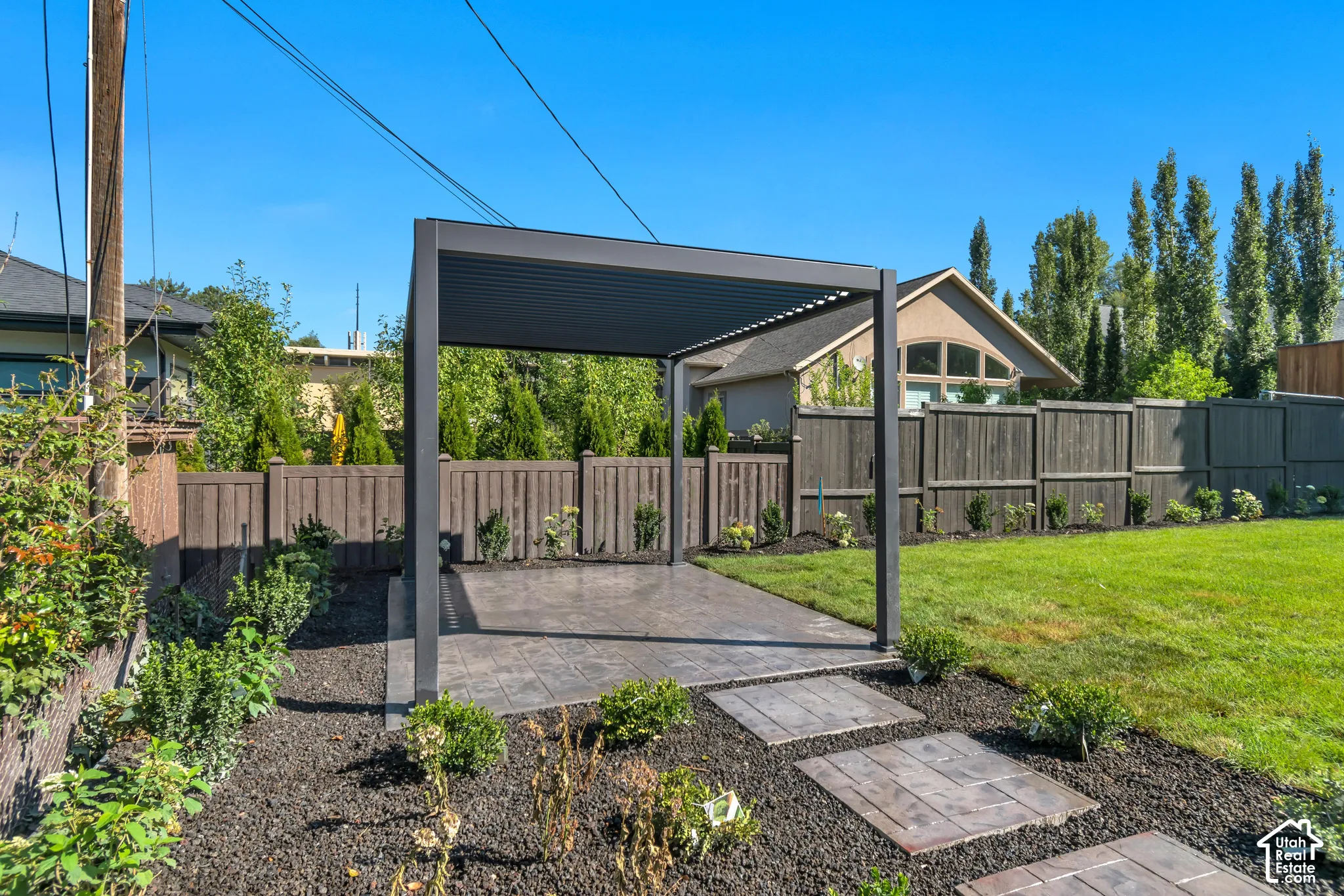 Outdoor patio space featuring a dark-toned pergola, stamped concrete patio, and garden beds with integrated stepping stones