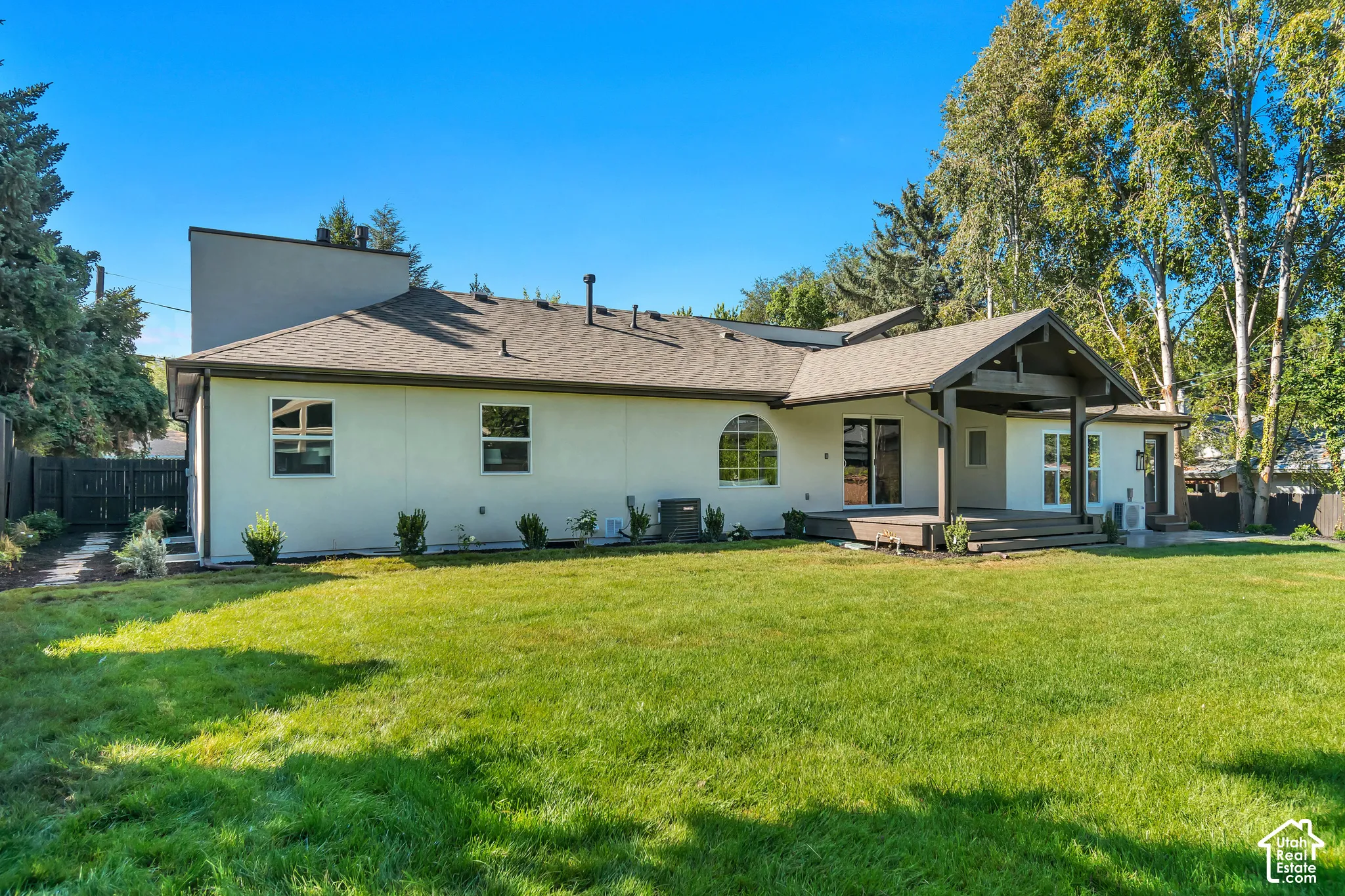 Expansive backyard featuring a manicured lawn, an extended wood-finish deck, and a covered patio area with dark wood-finish architectural accents
