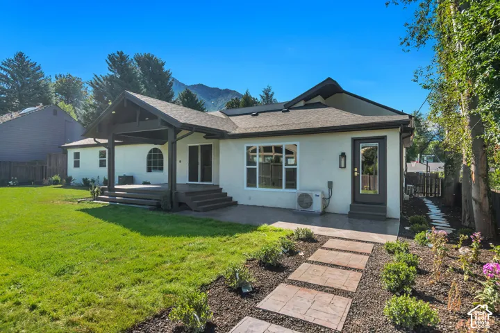 Rear exterior featuring a covered patio, expansive lawn, and mountain backdrop