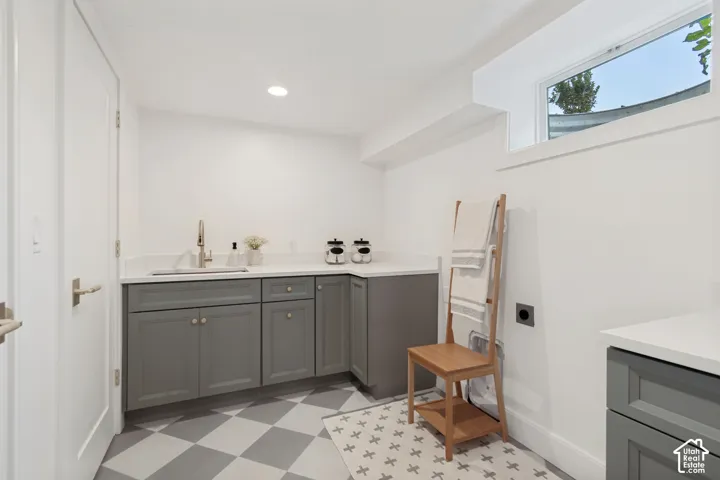 Laundry area featuring a built-in sink with a gooseneck faucet, gray cabinetry, light-toned countertops, and a checkered floor pattern