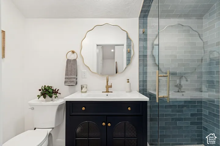 Bathroom featuring a frameless glass shower enclosure with subway tile surround, a dark wood vanity with a white countertop, and a scalloped mirror with a gold-tone frame