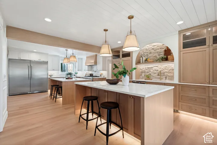 Spacious kitchen featuring two islands with white countertops, light wood-finish cabinetry, and recessed lighting