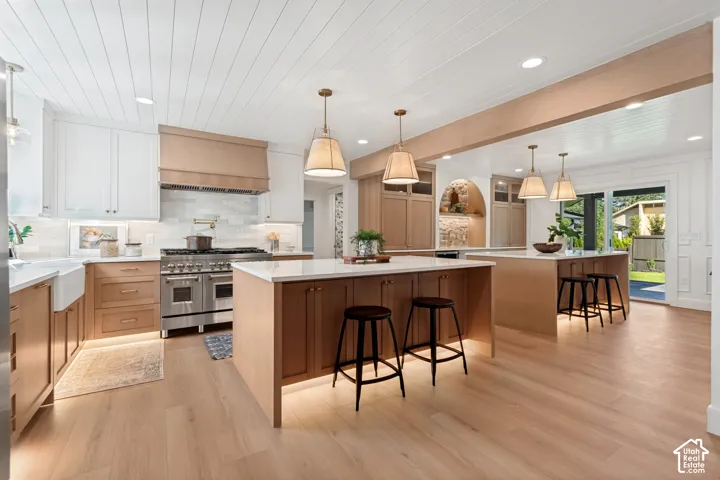 Gourmet kitchen with wood-finish flooring, two-tone cabinetry, stainless steel range, white farmhouse sink, and two kitchen islands with pendant lighting