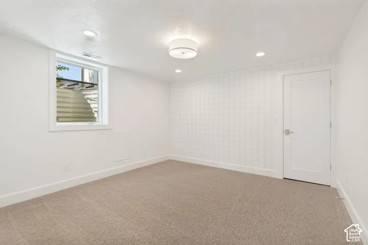 Spacious room featuring neutral carpet flooring, a single window, recessed lighting, a modern ceiling light fixture, and a solid panel door with brushed nickel hardware