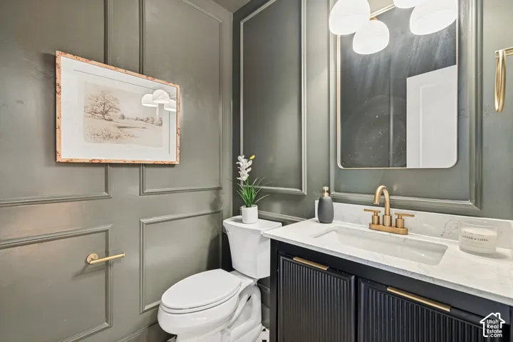 Powder room featuring panel molding, a white vanity with a rectangular basin, gold-toned faucet, and a contemporary wall-mounted light fixture