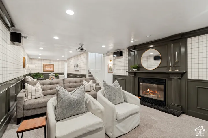 Carpeted recreation room featuring an elegant fireplace with a dark mantel, detailed wainscoting, recessed lighting, and a ceiling-mounted projector