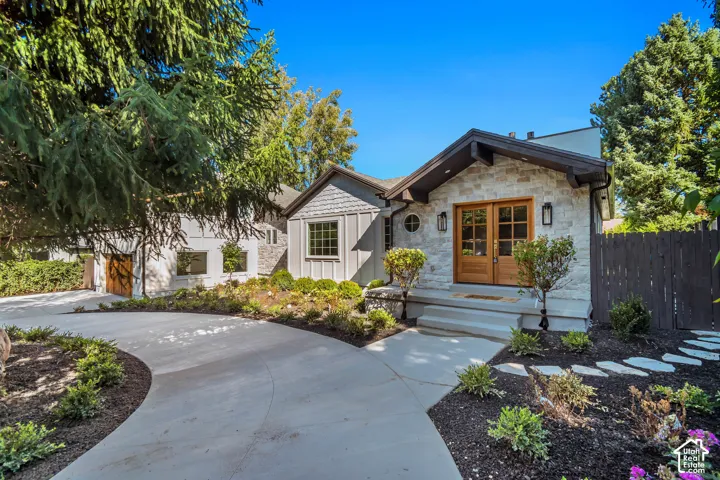 Stone facade exterior with dual wood entry doors, a curved concrete driveway, and established landscaping