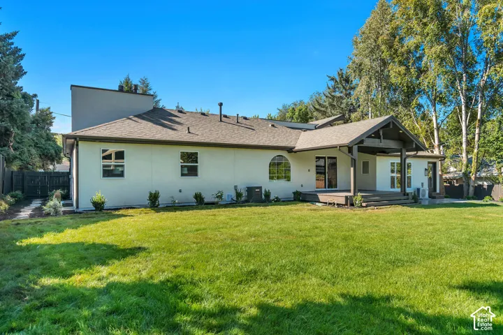 Expansive backyard featuring a manicured lawn, an extended wood-finish deck, and a covered patio area with dark wood-finish architectural accents