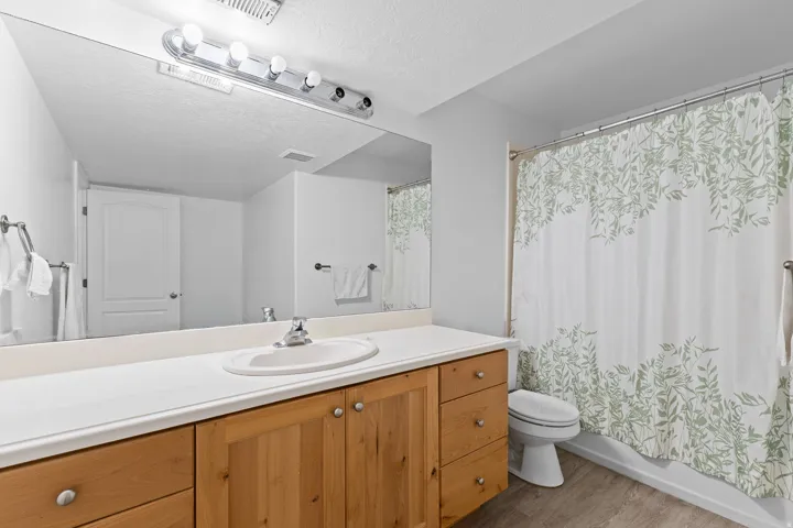 Bathroom featuring a light wood-finish vanity with a white countertop and integrated sink, a large wall-mounted mirror, and a shower with a white tub surround