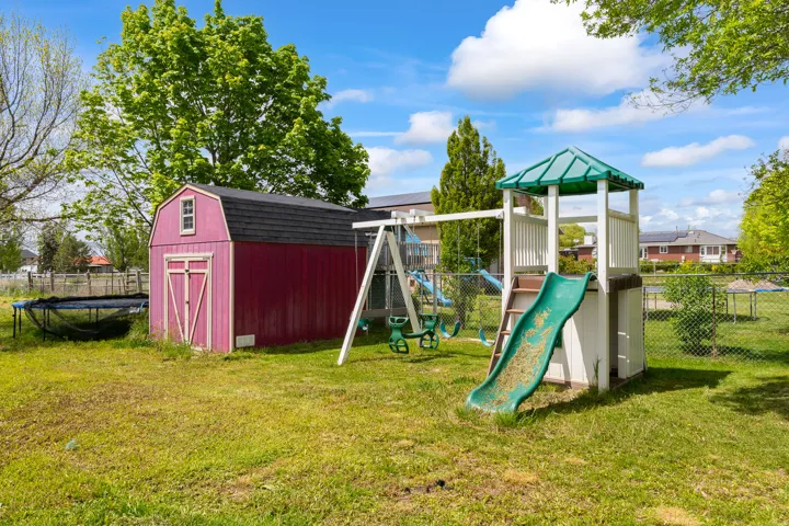 Expansive rear yard featuring a red storage shed with a gambrel roof and a playset with a slide