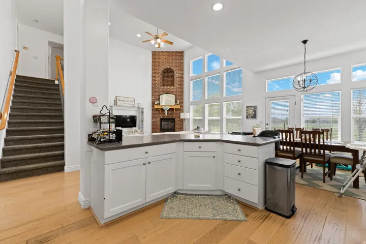 Open-concept living area with wood-finish flooring, a brick-accented fireplace, and a kitchen island featuring white cabinetry