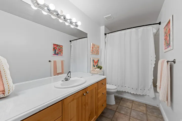 Bathroom featuring a light wood-finish vanity with a single basin, a white countertop, and a vanity mirror with overhead lighting