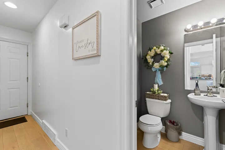 Powder room with a pedestal sink, wall-mounted mirror, and wood-finish flooring