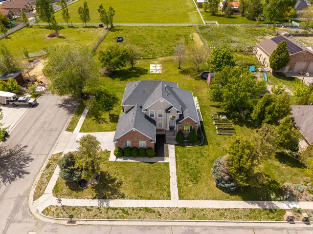 Two-story residence featuring a brick and siding exterior, front lawn, mature trees, and raised garden beds