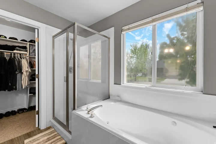 Soaking tub with brushed nickel fixtures, a glass-enclosed shower, and an adjacent walk-in closet with built-in shelving