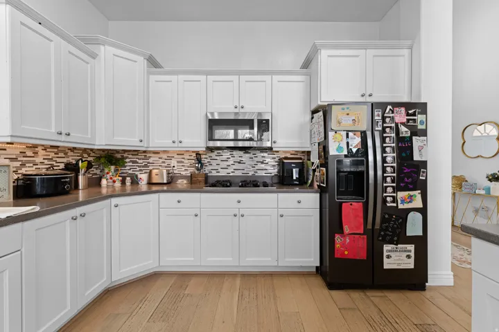 Kitchen featuring white shaker cabinetry, stainless steel appliances, mosaic tile backsplash, wood-finish flooring, and ample counter space