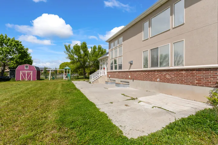 Expansive lawn featuring a storage shed, concrete patio, and a swing set