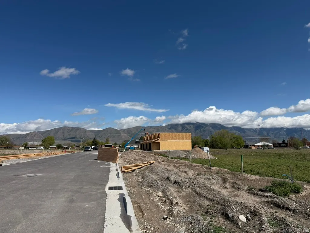 New construction framing visible, featuring a mountain backdrop, paved street, and developing lot