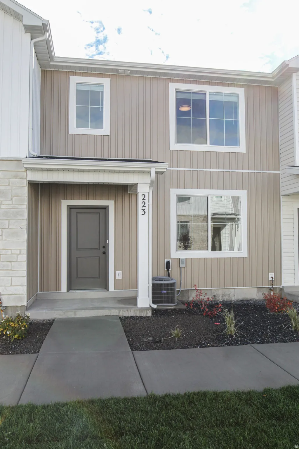 Contemporary townhouse exterior featuring a covered entry, vertical siding, stone veneer accents, multiple windows, and a paved walkway