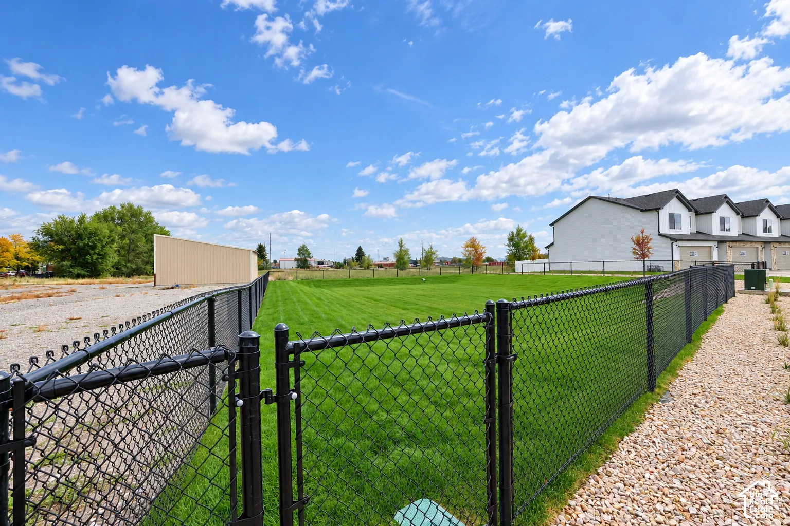 Fenced backyard featuring a manicured lawn, gravel perimeter, and metal chain-link enclosure
