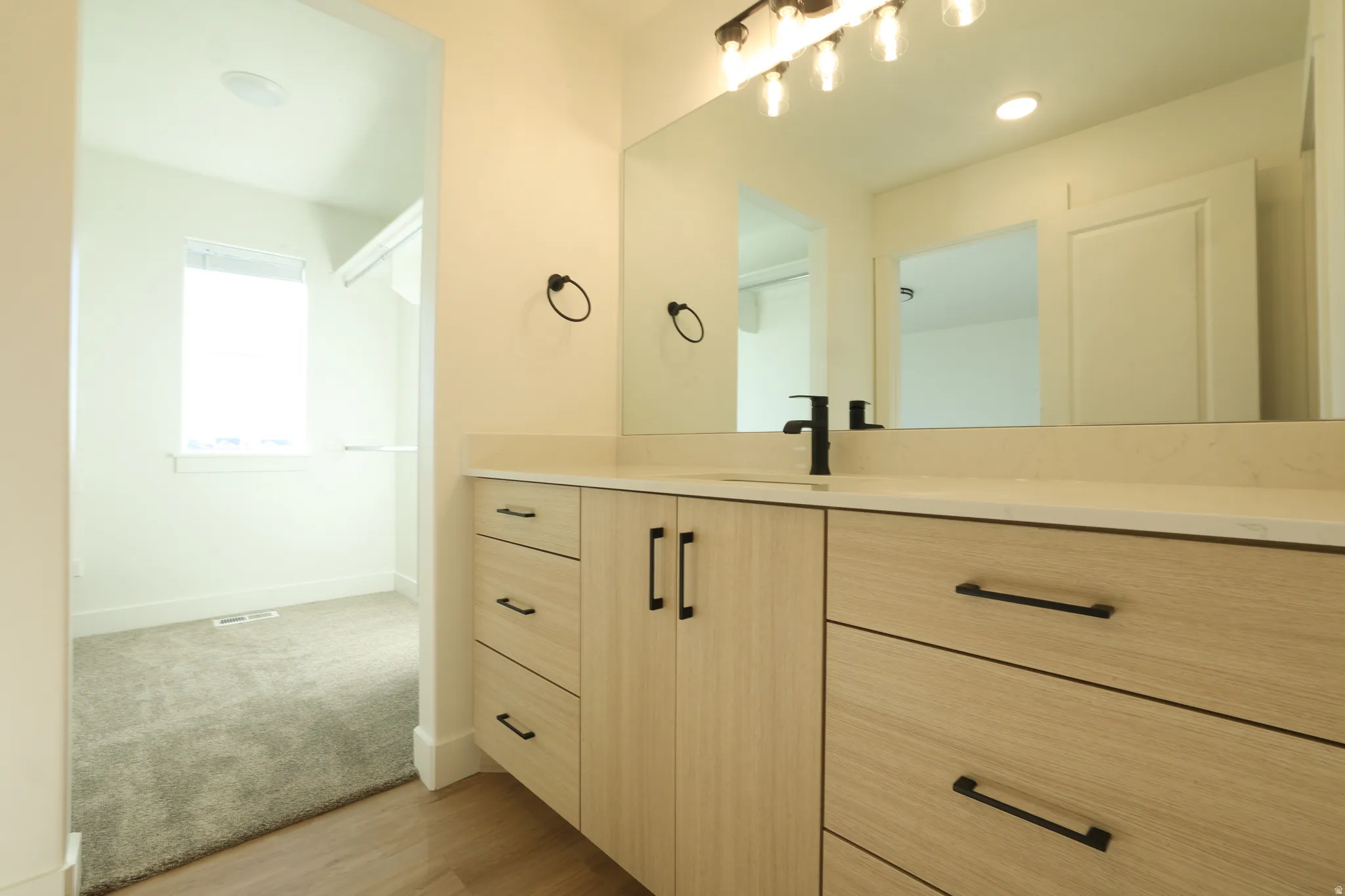 Modern vanity featuring light wood-finish cabinetry with matte black hardware, a light-toned countertop, and a rectangular sink with a matte black faucet