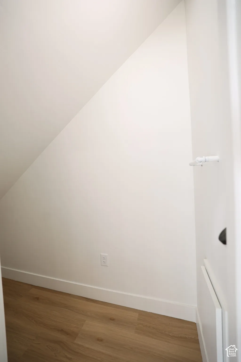 Under-stair storage area with wood-finish flooring, white baseboards, and a white wall finish