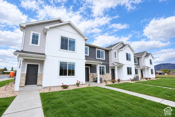 Multi-family exterior featuring mixed-material siding, stacked-stone accents, concrete walkways, and manicured lawn areas