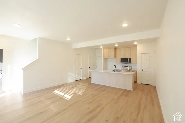 Open-concept living space featuring wood-finish flooring, recessed lighting, a kitchen island with a built-in sink, and light wood cabinetry