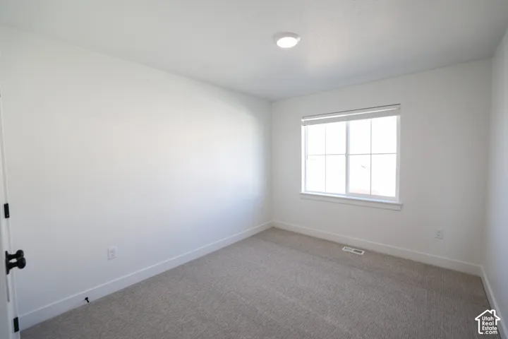 Neutral toned bedroom featuring light grey carpeting, white walls, and a recessed ceiling light