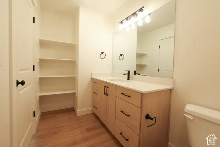 Modern bathroom featuring wood-finish flooring, a light wood-tone vanity with black hardware, a rectangular undermount sink with a black faucet, and a large mirror with a multi-bulb light fixture