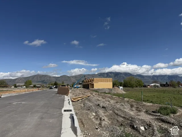 New construction framing visible, featuring a mountain backdrop, paved street, and developing lot