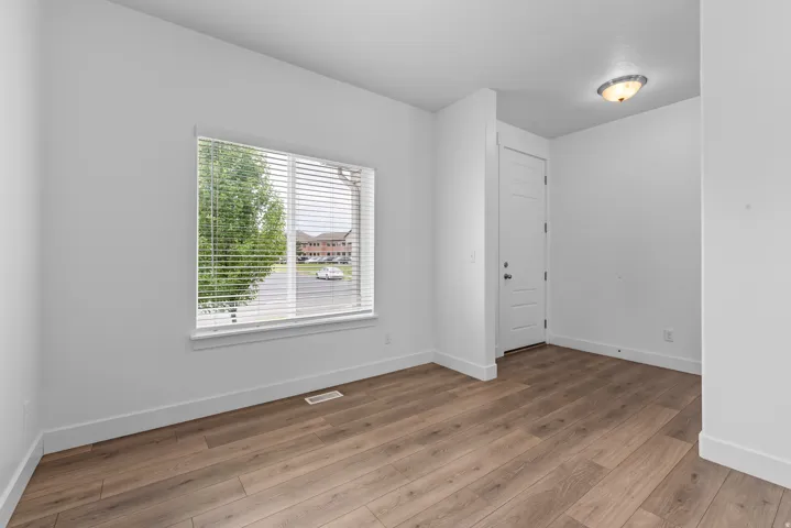 Bright room featuring a large window with blinds, wood-finish flooring, a contemporary ceiling light fixture, and a paneled interior door