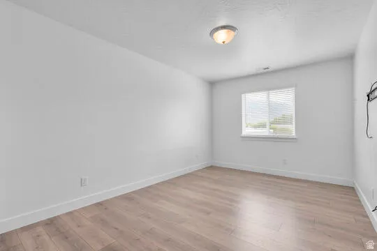 Spacious room featuring light wood-finish flooring, white baseboards, and a large window with blinds