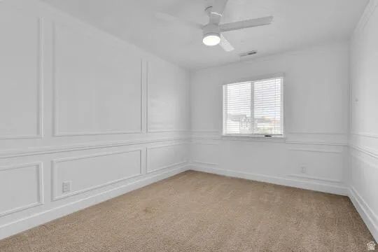 Bright interior space featuring a window with blinds, a ceiling fan with integrated lighting, and extensive white wall paneling