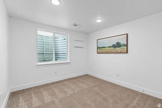 Carpeted interior space featuring a window with a window well, recessed lighting, and white baseboards