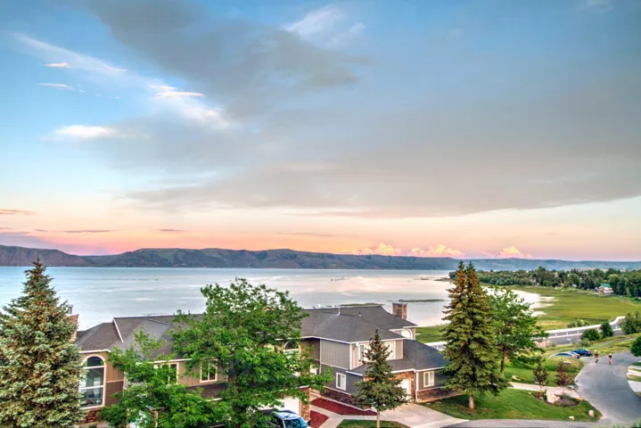 Expansive water and mountain scenery from a multi-story residence featuring a stone and siding exterior, a multi-pitch roof, and mature landscaping
