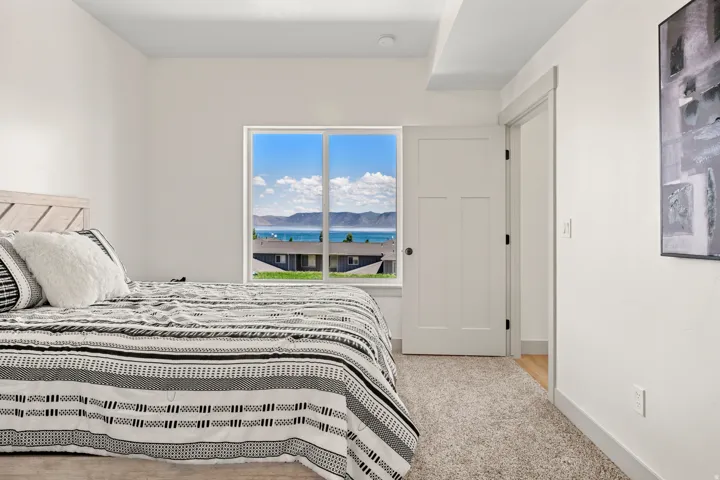 Spacious room featuring a large window with water and distant mountain scenery, neutral wall paint, white trim, and light-colored carpeting
