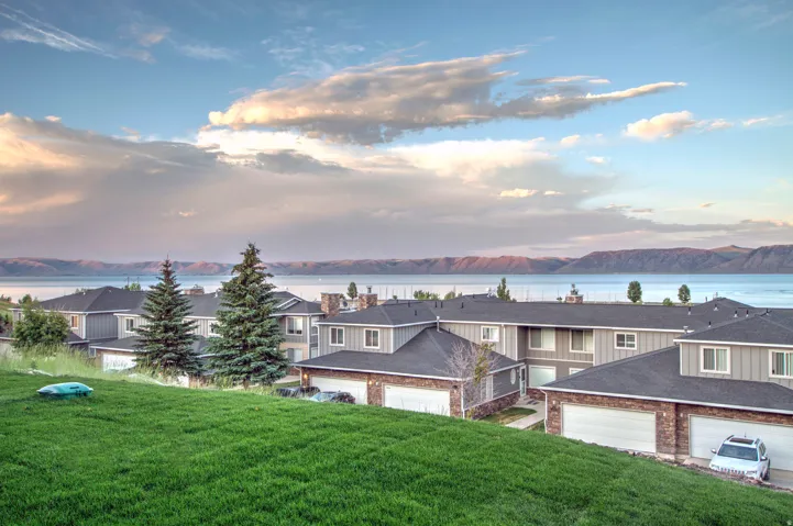 Residential buildings featuring grey siding and brick accents, individual attached garages, and a backdrop of a large body of water with distant mountains