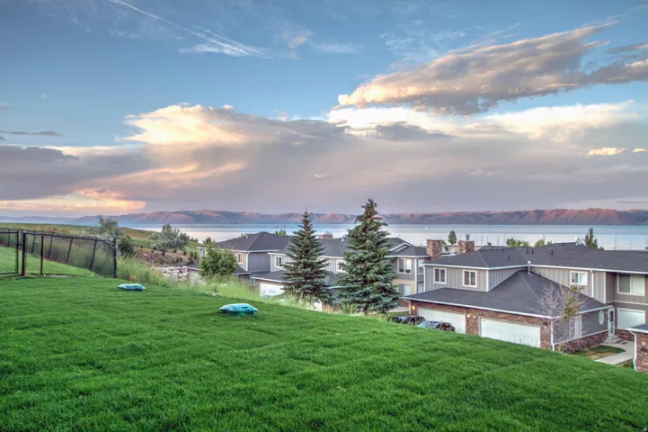 Expansive green lawn with a chain-link fence, offering distant water and mountain scenery
