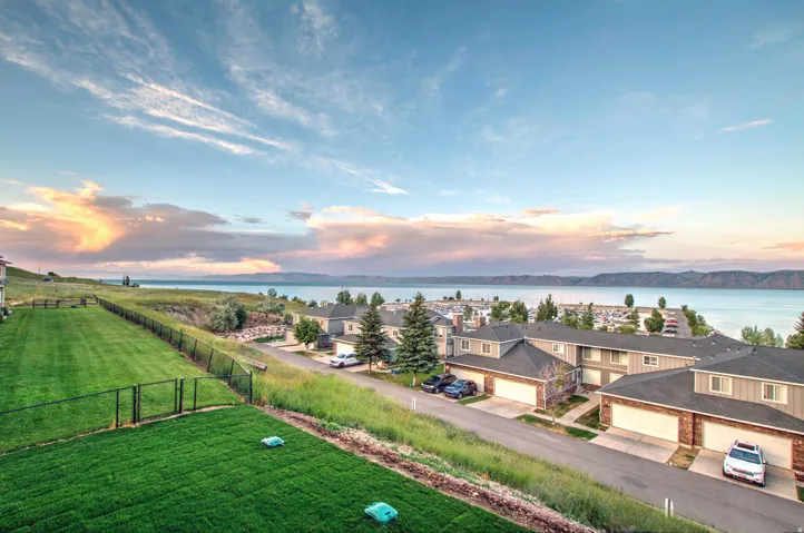 Expansive grassy area with a black metal fence, overlooking a body of water with distant mountains