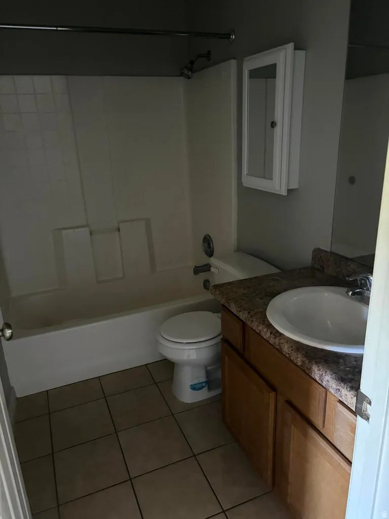 Bathroom featuring a white tub with shower surround, a white toilet, and tile flooring