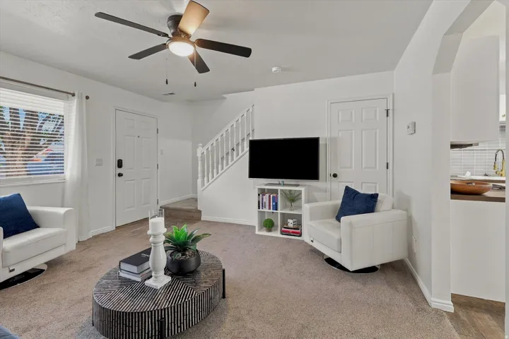 Carpeted living area featuring a ceiling fan with light, white trim, and a window with blinds