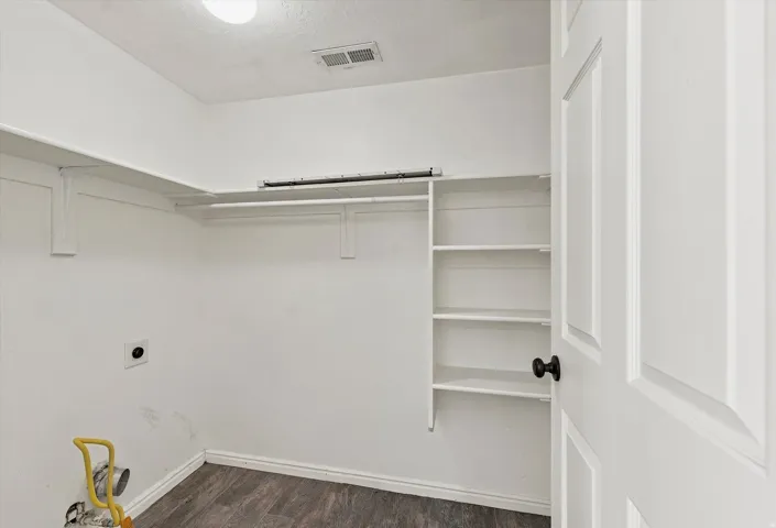 Laundry area featuring white walls, wood-finish flooring, a white paneled door with a matte black knob, and built-in shelving and hanging rods
