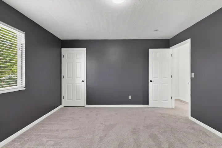 Spacious room featuring dark gray walls, light gray carpet flooring, white baseboards, and a single window with horizontal blinds