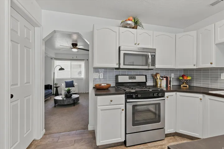 Kitchen featuring white cabinetry, stainless steel appliances, dark countertops, and a gray subway tile backsplash