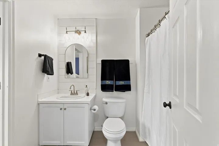 Bathroom featuring a single vanity with white cabinetry and countertop, an arched mirror, and shiplap-style accent wall