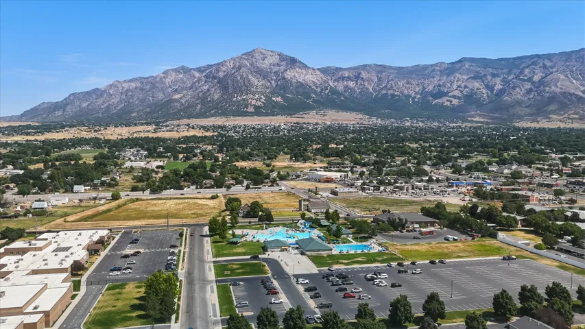 Expansive aerial capturing a mountain backdrop, a community aquatic center with multiple pools, and mature trees throughout the surrounding area