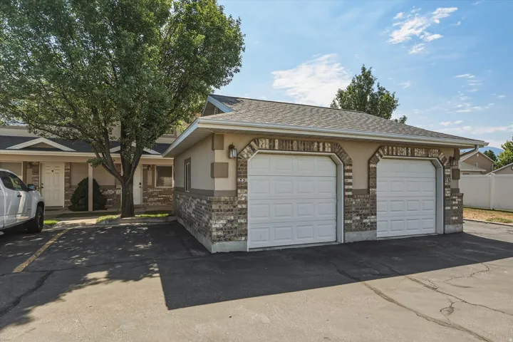 Two-car garage with arched brick detailing, stucco siding, and complementary outdoor lighting fixtures