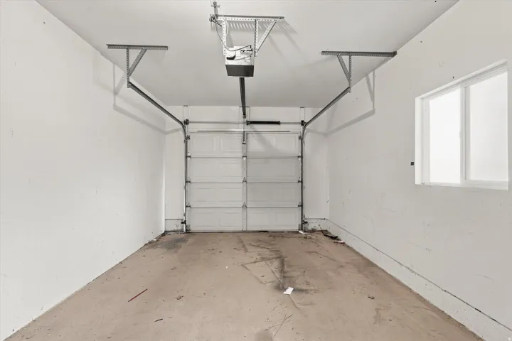 Single-car garage featuring a roll-up door, automatic opener, concrete flooring, and a window for natural light