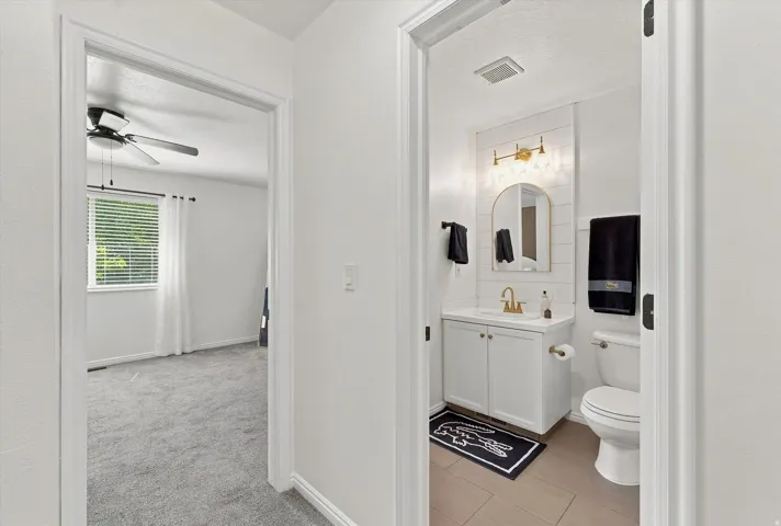Bathroom featuring a white vanity with a gold-toned faucet, an arched mirror, and a tiled accent wall